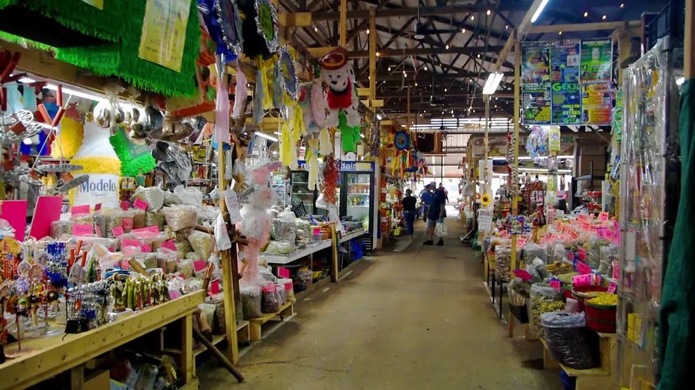 Interior de Azteca Farmers Market lleno de puestos de piñatas, dulces y artesanías